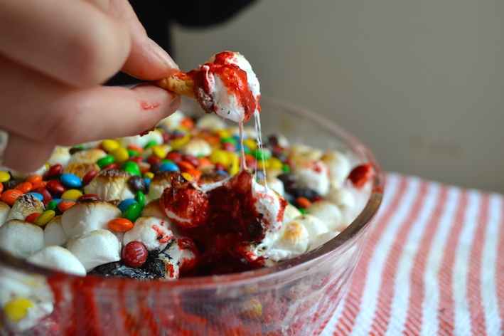 a giant bowl full of red velvet s'mores dip topped with marshmallows and m&m chocolate candies