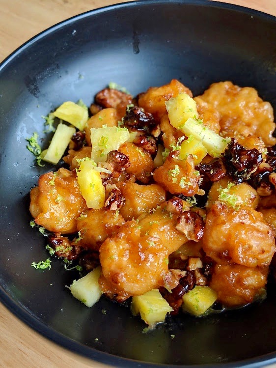 A bowl of homemade crispy rock shrimp with candied walnuts, pineapple slices and lime zest