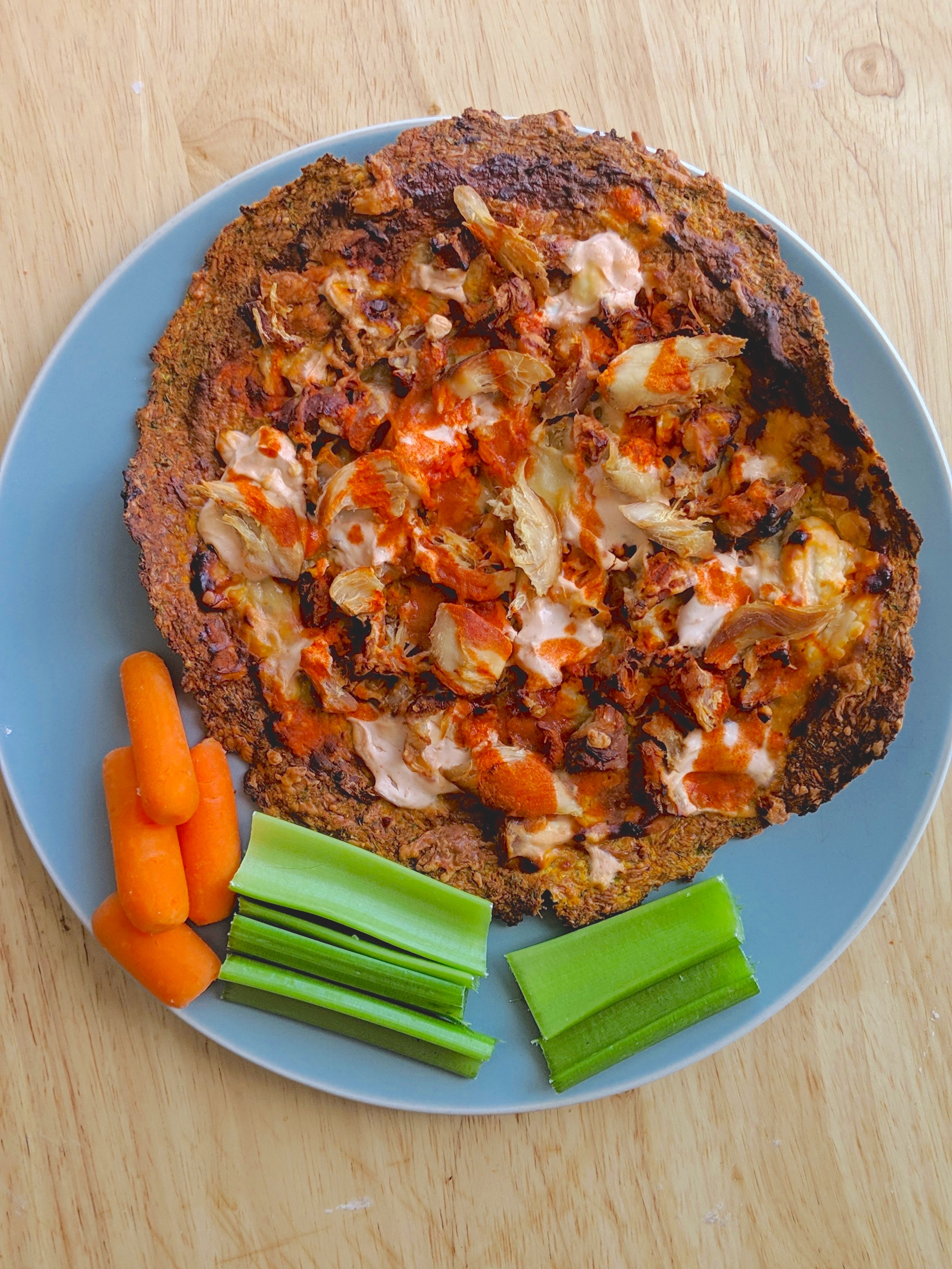 grain-free buffalo chicken pizza on a blue plate with a side of carrots and celery