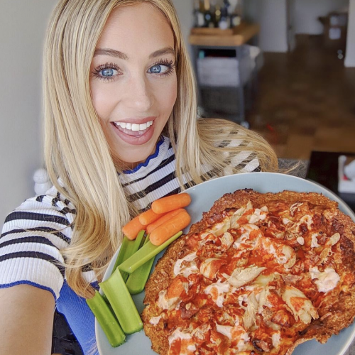 woman snacking on carrots and celery with a thin crust buffalo chicken pizza on a blue plate