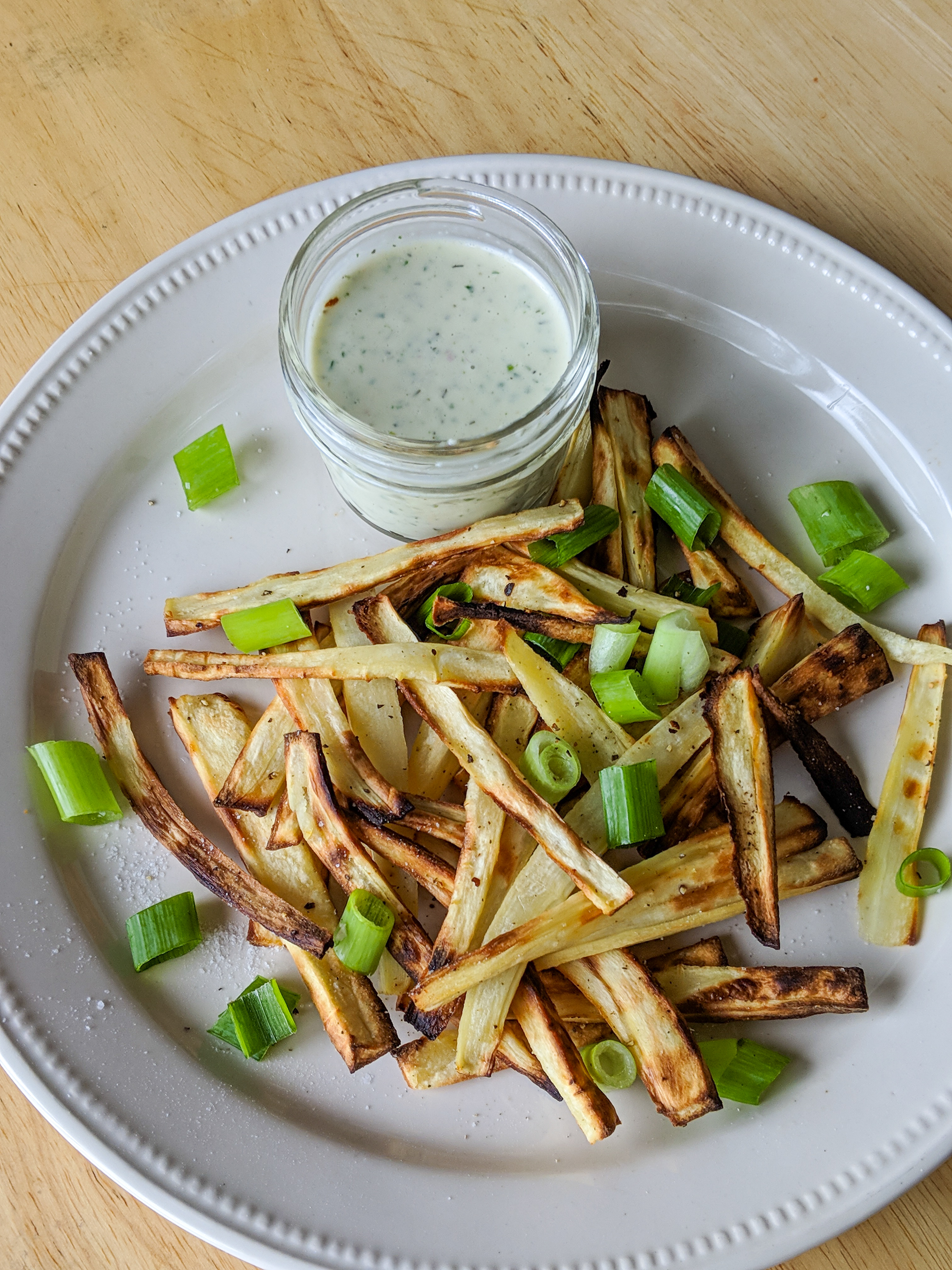 a plate of parsnip fries with scallions and a side of homemade greek yogurt ranch dressing