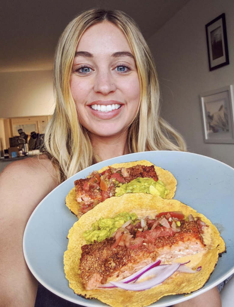 Skyler Bouchard holding a plate full of salmon tacos with a crispy fried exterior, guacamole, salsa and a corn tortilla