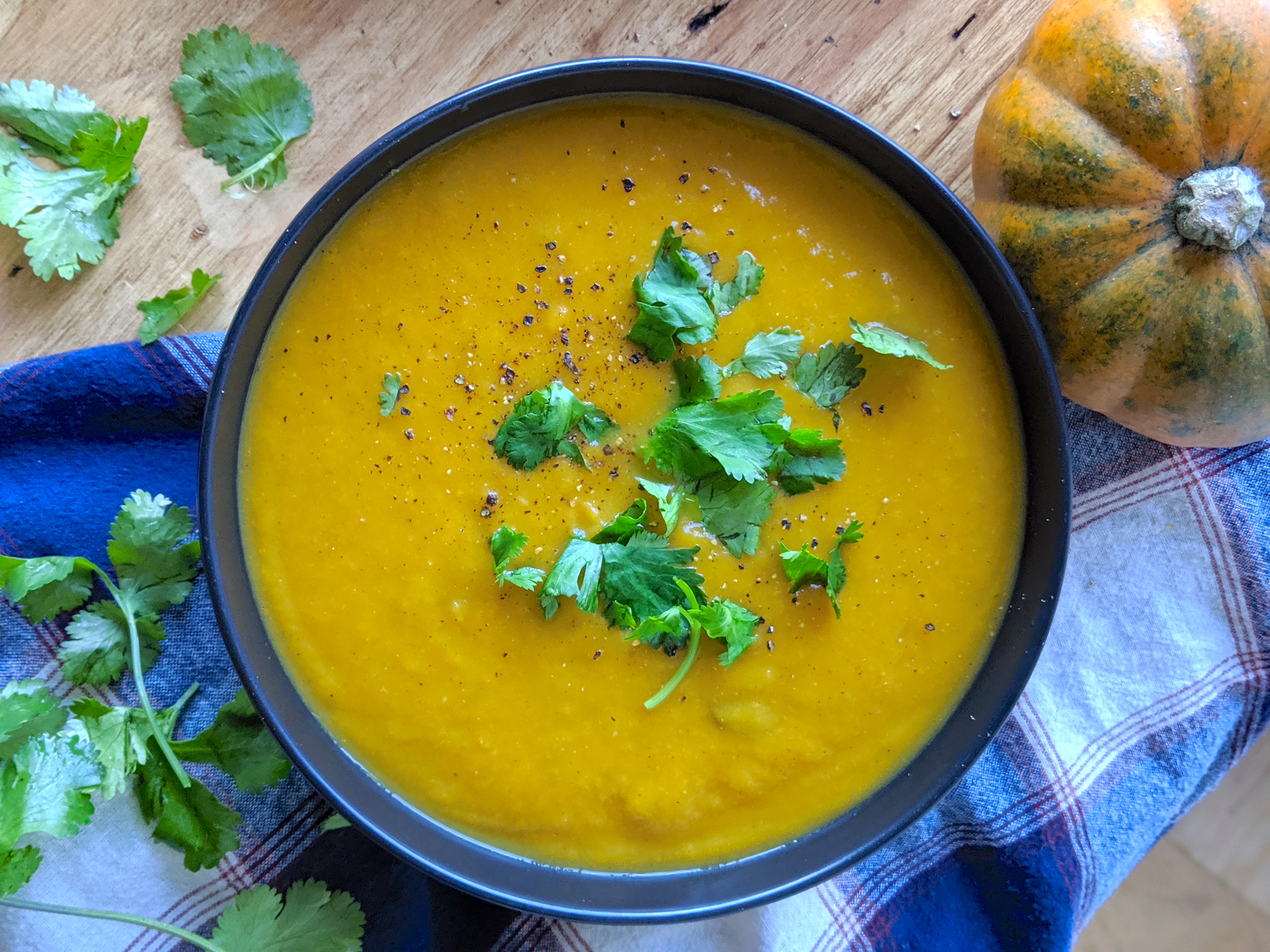 a big bowl of butternut squash apple soup with cilantro and black cracked pepper