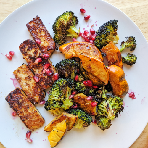Plate of seared golden brown pumpkin spice halloumi with broccoli and acorn squash and pomegranate