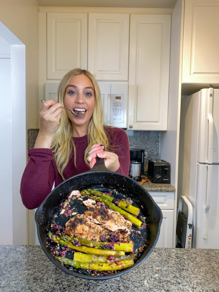 Skyler Bouchard with a cast iron skillet full of crispy almond cursted salmon on a bed of green beans and cranberries