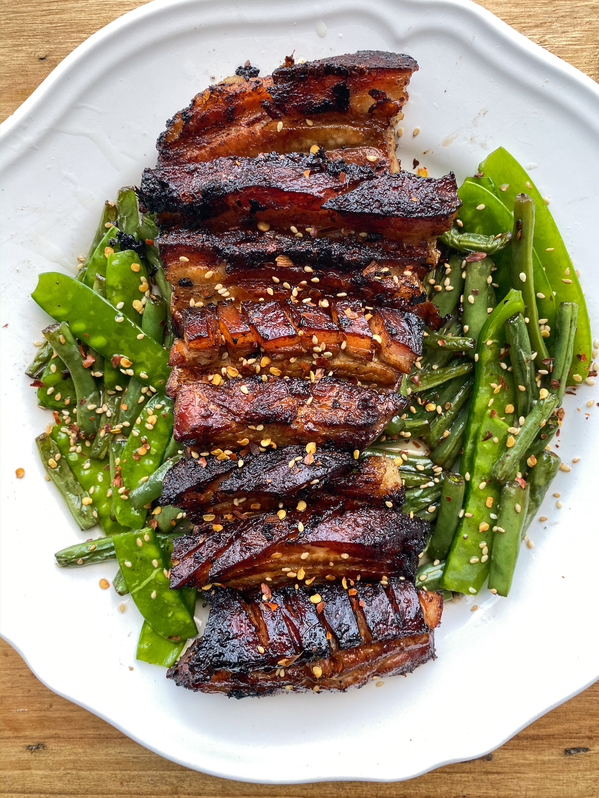 a plate of crispy pork belly with green beans, snap peas and sesame seeds