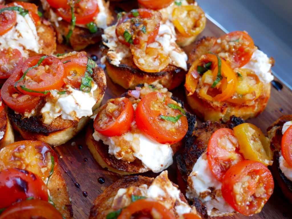 Platter of bruschetta with creamy burrata, garlic bread, and marinated cherry tomatoes – fresh tomato season recipe for summer entertaining.