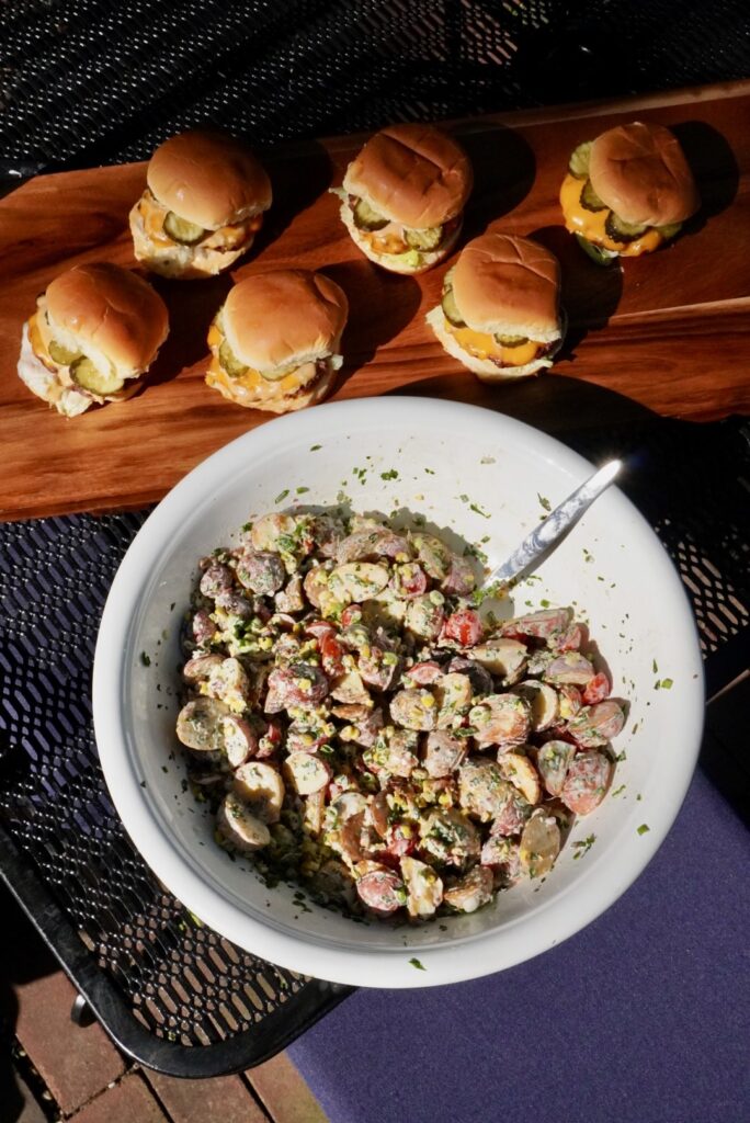 roasted potato salad with corn, herbs and bacon and a side of cheeseburgers at a cookout