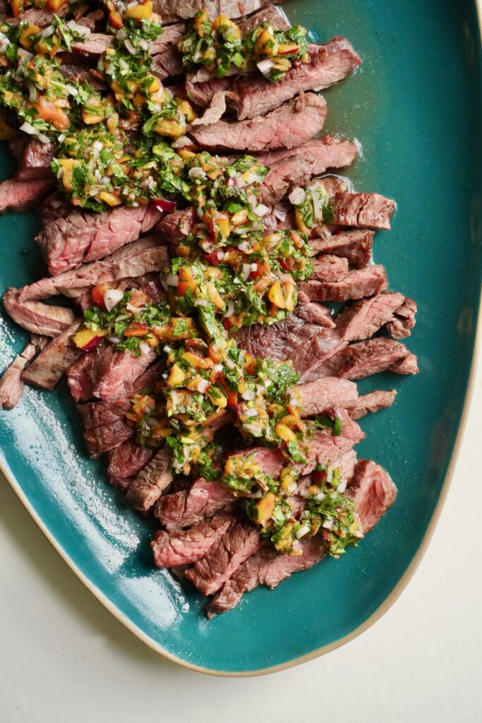 Sliced skirt steak with peach chimichurri sauce and fresh herbs