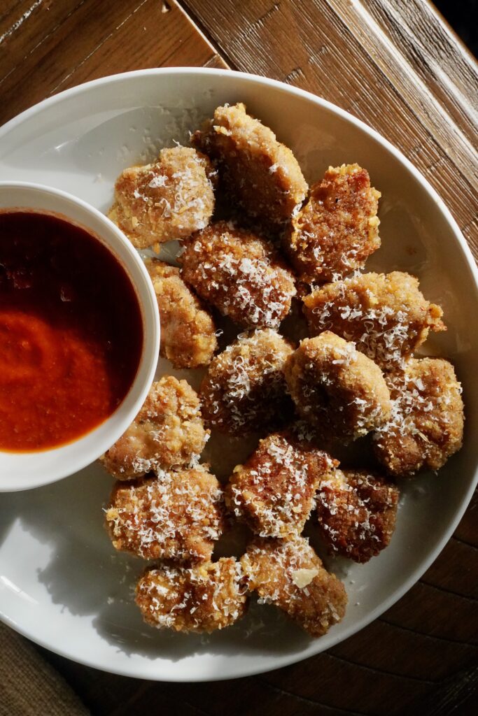 Plate of garlic parmesan turkey nuggets sprinkled with Parmesan and served with a bowl of marinara sauce.
