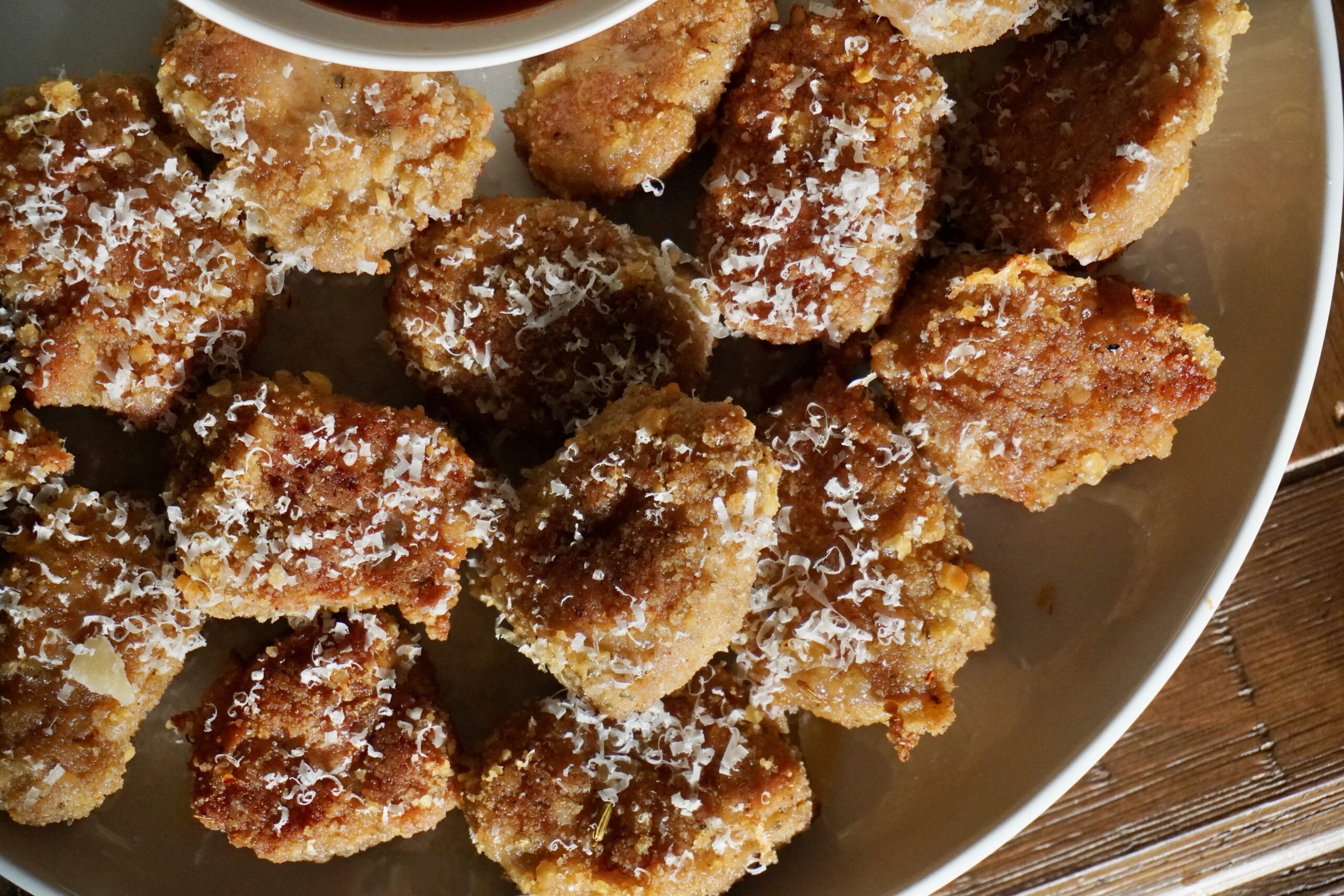 Close-up of golden brown baked turkey nuggets on a white plate with Parmesan on top.
