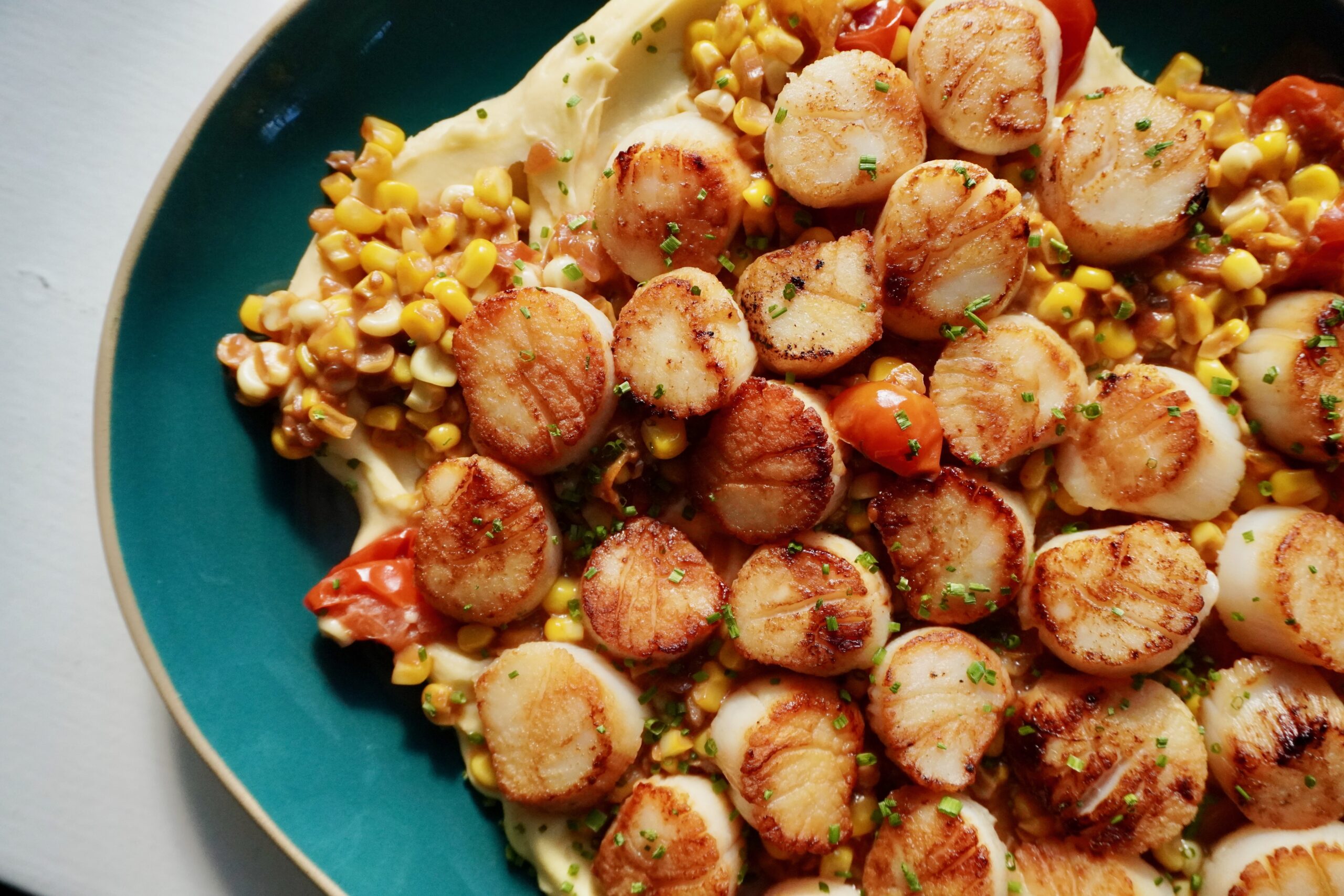 Family style seared scallops plated with parsnip purée and corn and tomatoes