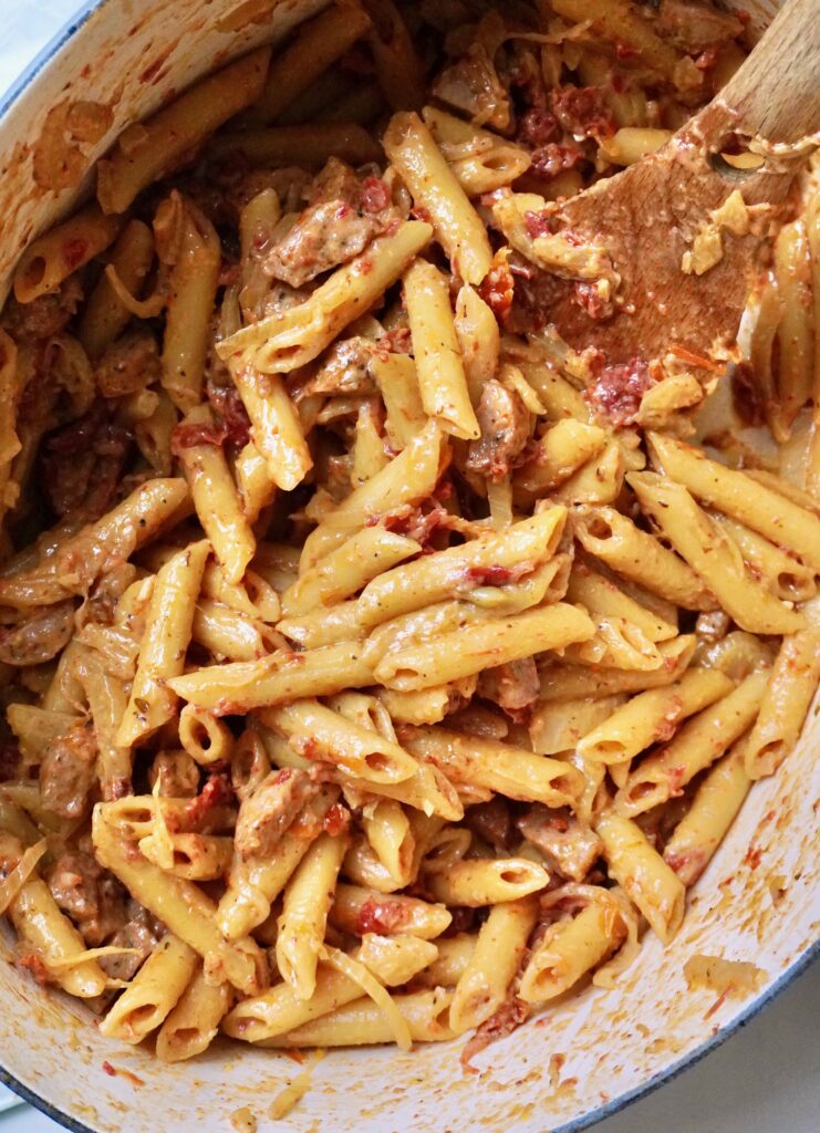 Close-up of finished creamy chicken sausage, fennel, and sun-dried tomato penne in a Dutch oven
