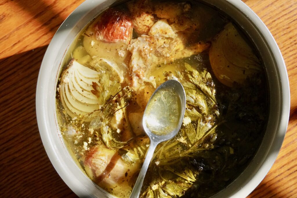 Slow cooker filled with chicken bones, herbs, and vegetables for stock