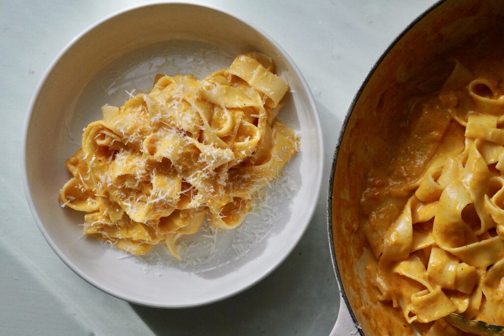 Cozy fall plate of honey nut squash Alfredo with brown butter and Parmesan shavings next to a skillet of pappardelle