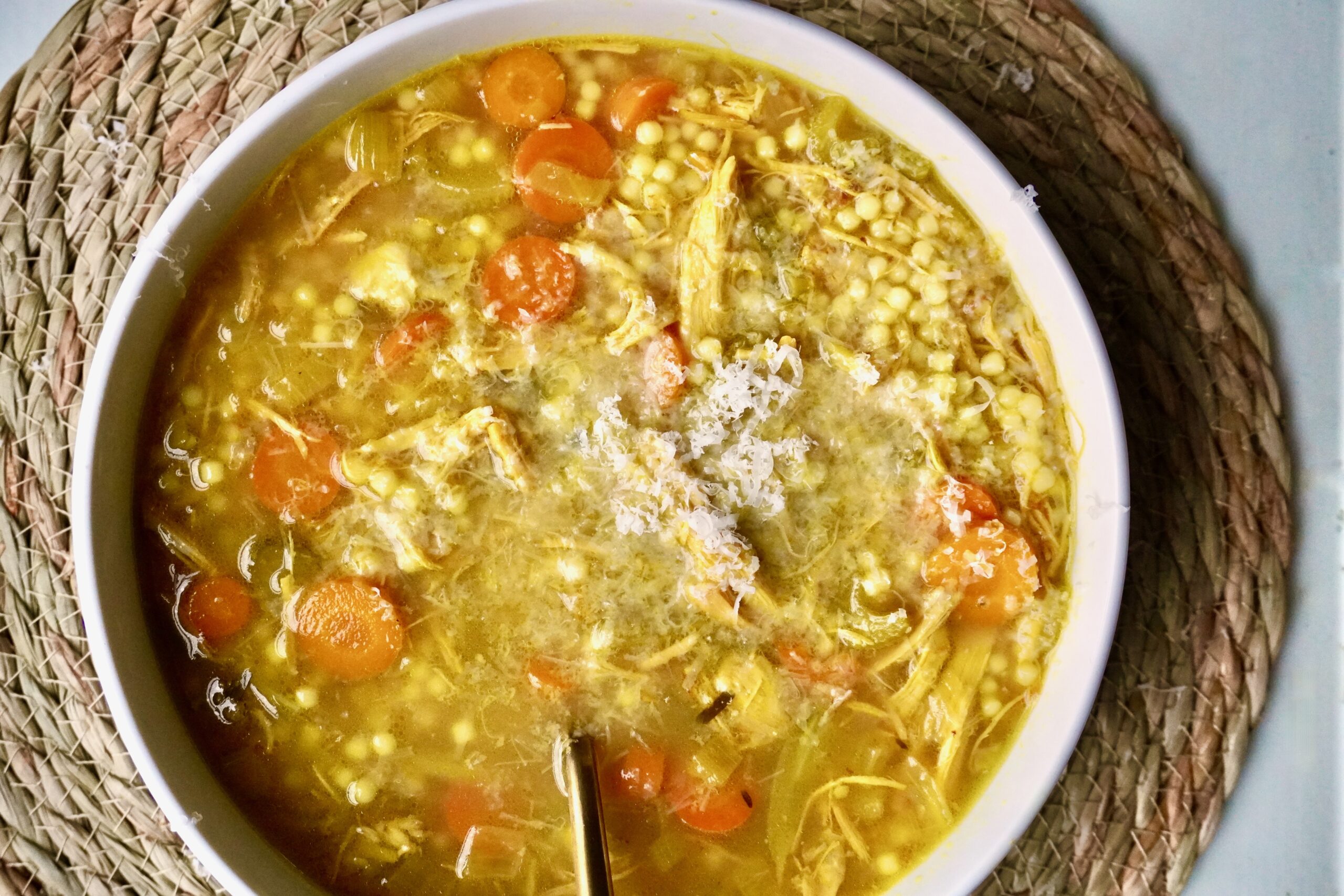 Overhead shot of steaming golden chicken soup with parmesan on top.