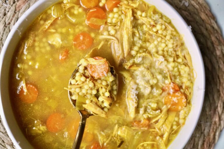 Close-up of garlic and turmeric chicken soup glowing with golden broth.