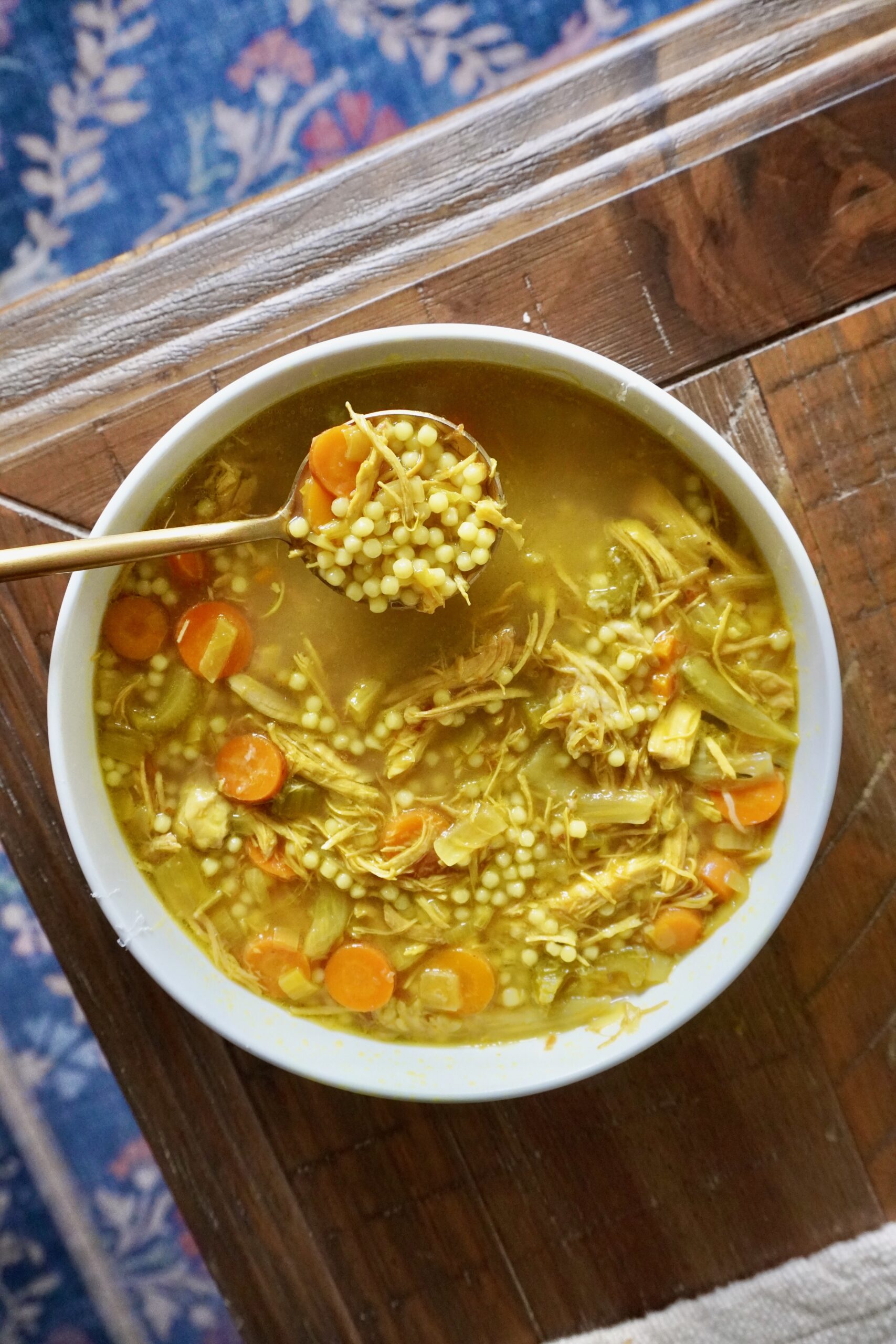 Spoon lifting a golden bite of pastina chicken soup with turmeric and herbs.Spoon lifting a golden bite of pastina chicken soup with turmeric and herbs.