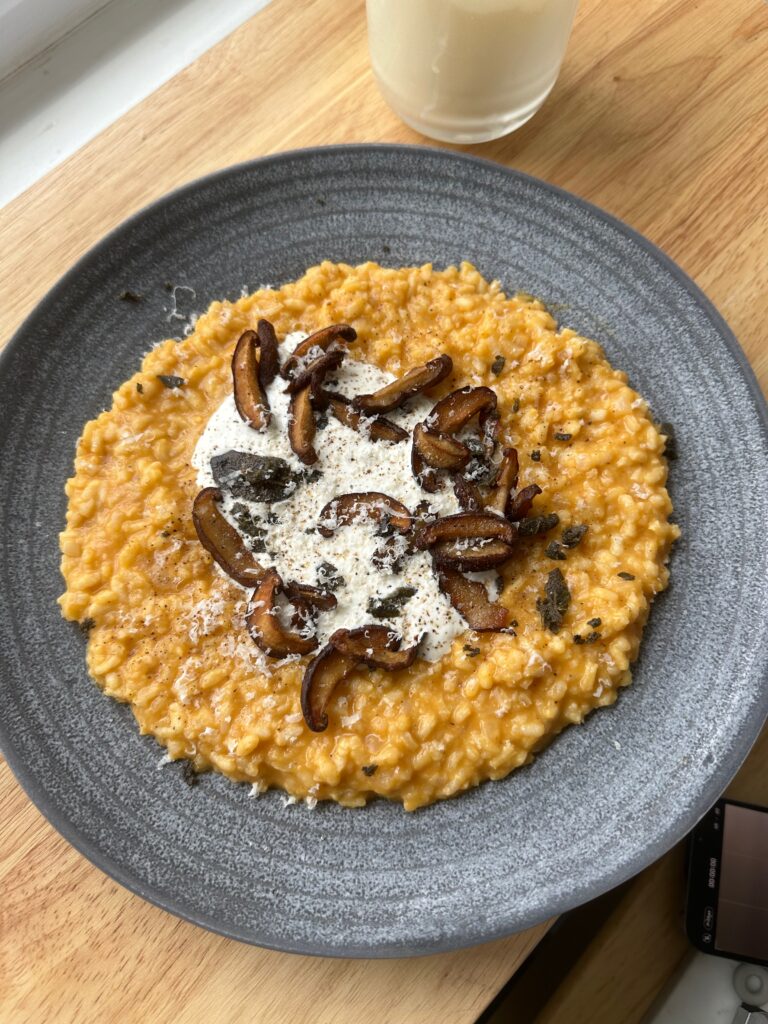 Bowl of creamy pumpkin risotto topped with stracciatella and crispy sage.