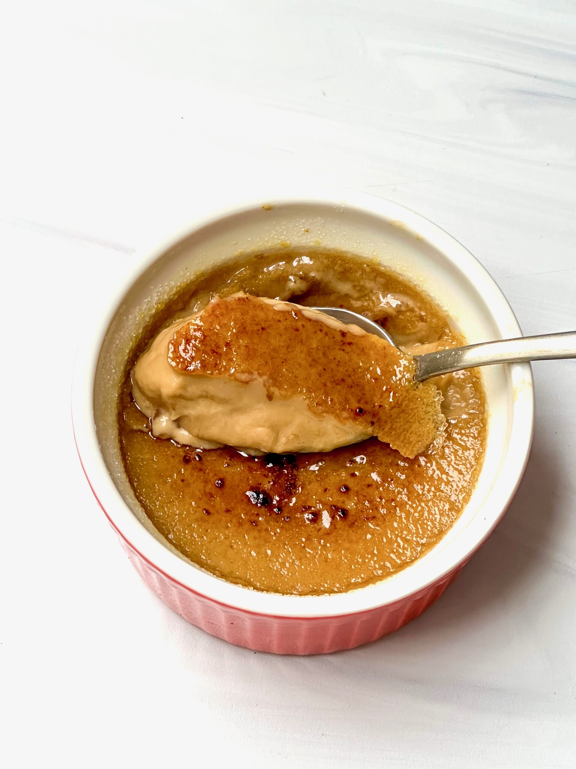 Spoon cracking through golden sugar on chai-infused crème brûlée.