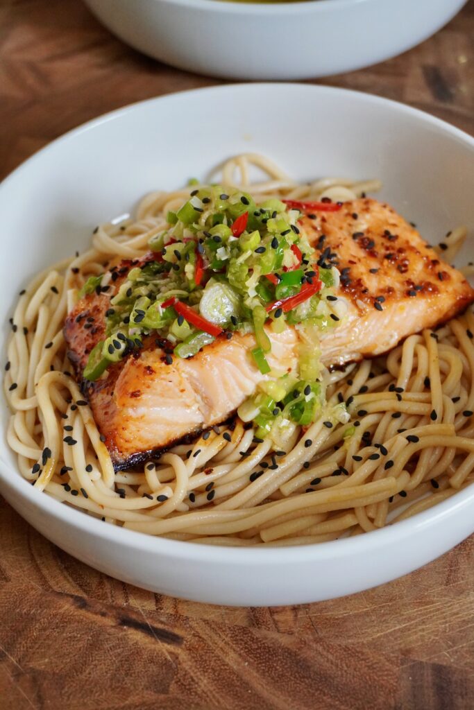 a close up image of roasted salmon over udon noodles