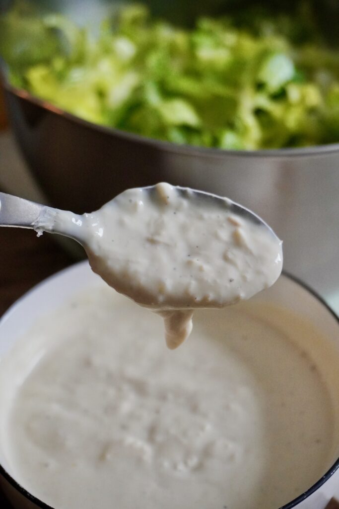 creamy high-protein greek yogurt dressing drizzling from a spoon in a container