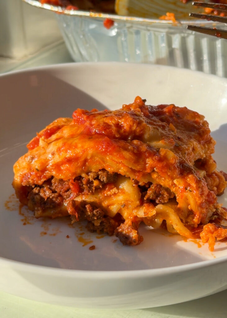 A perfect slice of high protein lasagna on a white plate, showing thick layers of pasta, rich meat sauce, and melted cheese