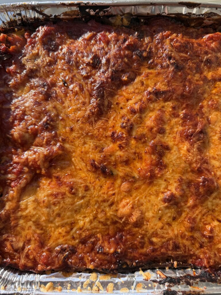 A 9x13 baking dish of cozy high-protein lasagna with a golden-brown, bubbling mozzarella and parmesan cheese crust