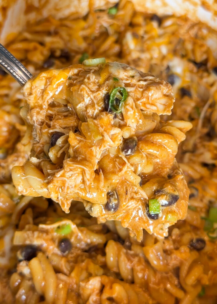 A wooden spoon lifting a generous, cheesy scoop of chicken taco pasta out of a pot