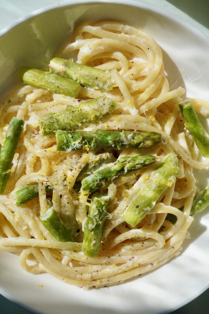 A closeup of bucatini pasta tossed in a creamy ricotta sauce with bright green asparagus