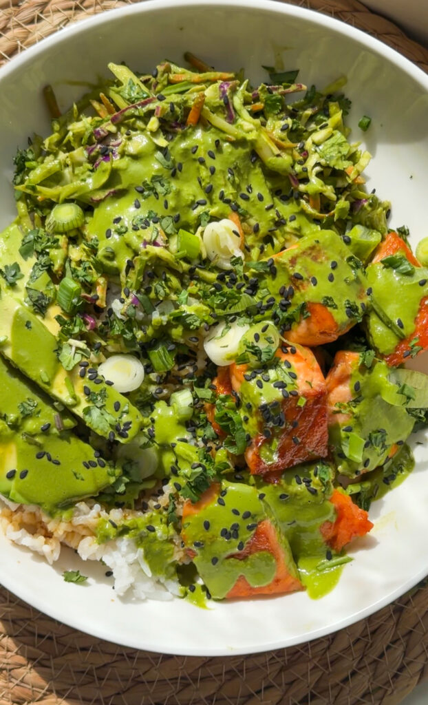 A vibrant bowl filled with white rice, green herb slaw, roasted salmon bites, and avocado, drizzled with creamy green goddess dressing