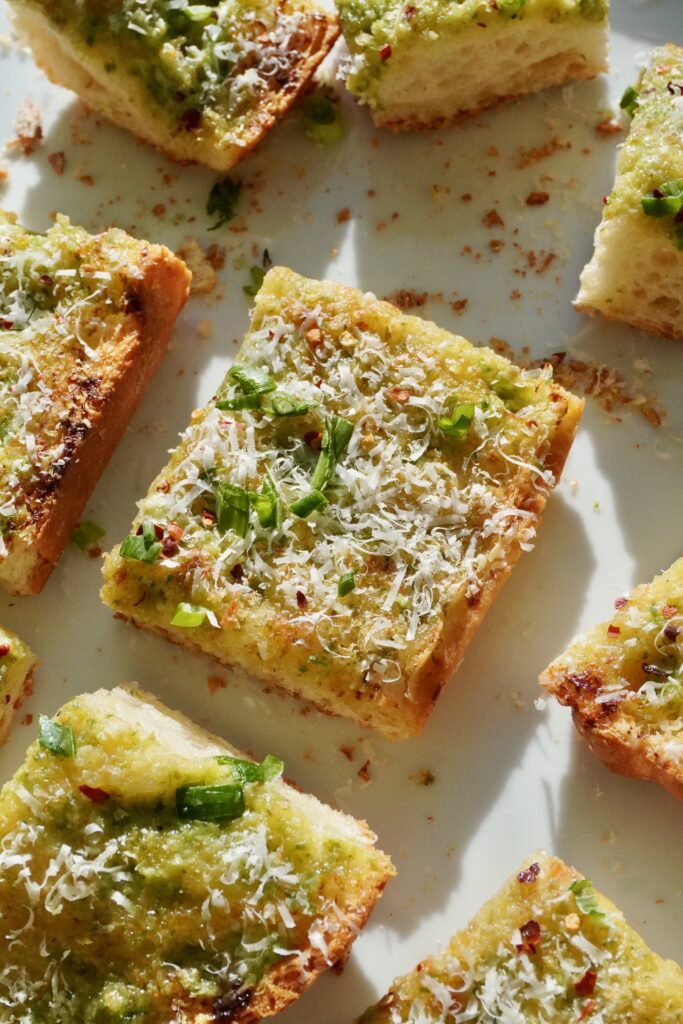 A loaf of ciabatta garlic bread with a bright green spring onion butter and melted Parmesan