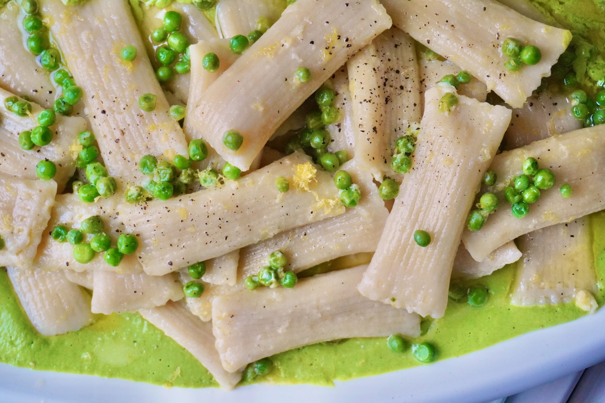 A shallow bowl featuring yellow cheese ravioli nestled on a vibrant green mint and basil pea purée