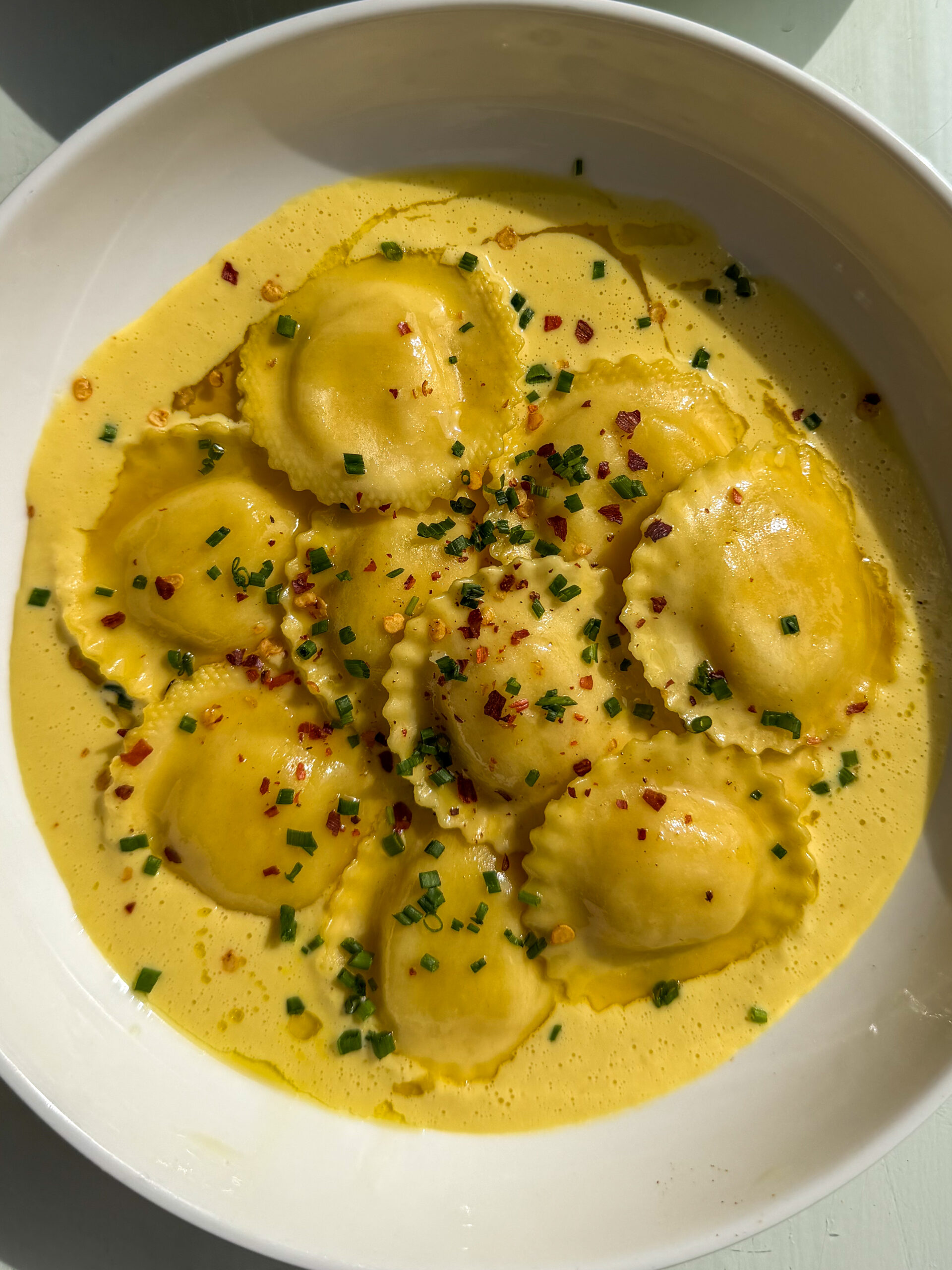 closeup of elegantly plated Ravioli with Corn Purée served with chives, chili flakes, and olive oil drizzle