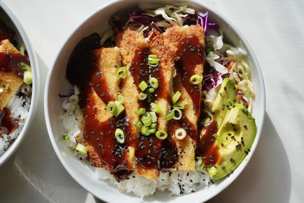 a close-up of oven-baked chicken katsu bowl served with rice, cabbage slaw, avocado slices, and sesame seeds