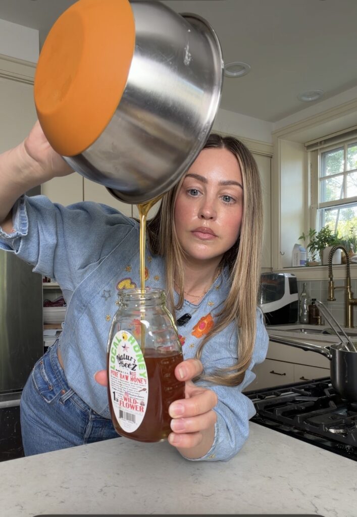 close up of homemade lavender honey with dried lavender buds being poured into a jar from a saucepan
