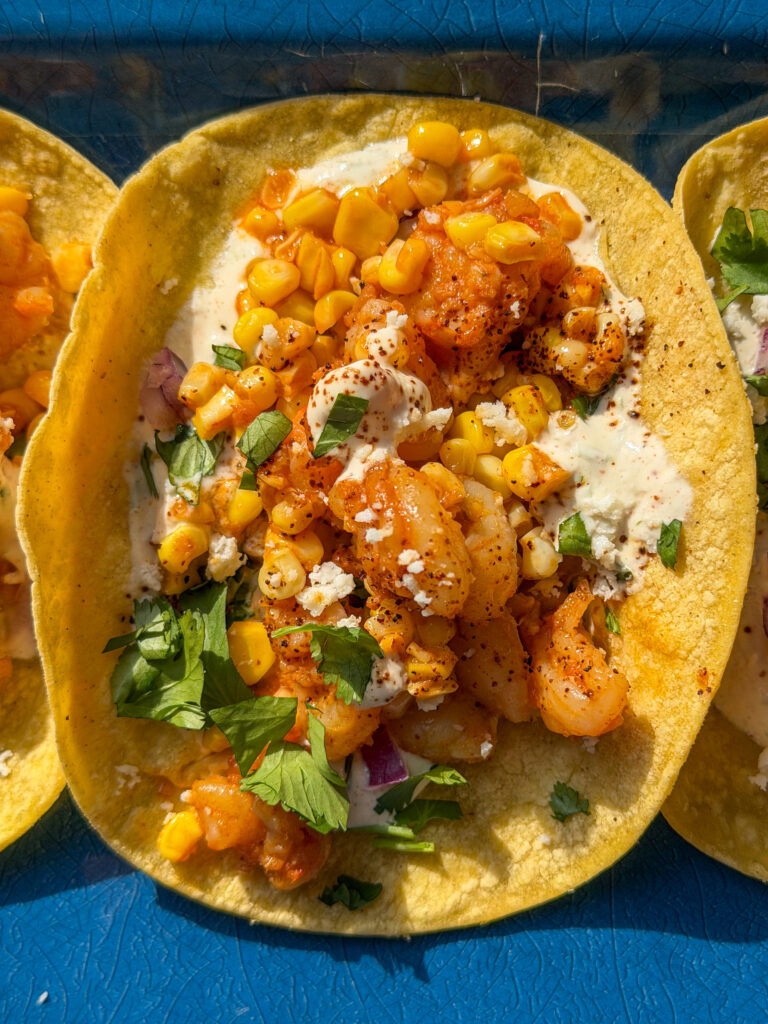 Mexican street-style Elote shrimp taco topped with cilantro lime crema, cotija cheese, and red onion
