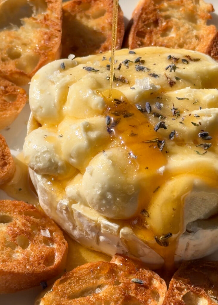 close-up of airy whipped brie piped into rind with lavender honey drizzle and served with crackers on a serving board