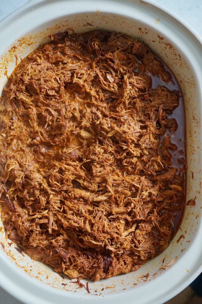 Overhead view of glossy BBQ pulled chicken in a white slow cooker