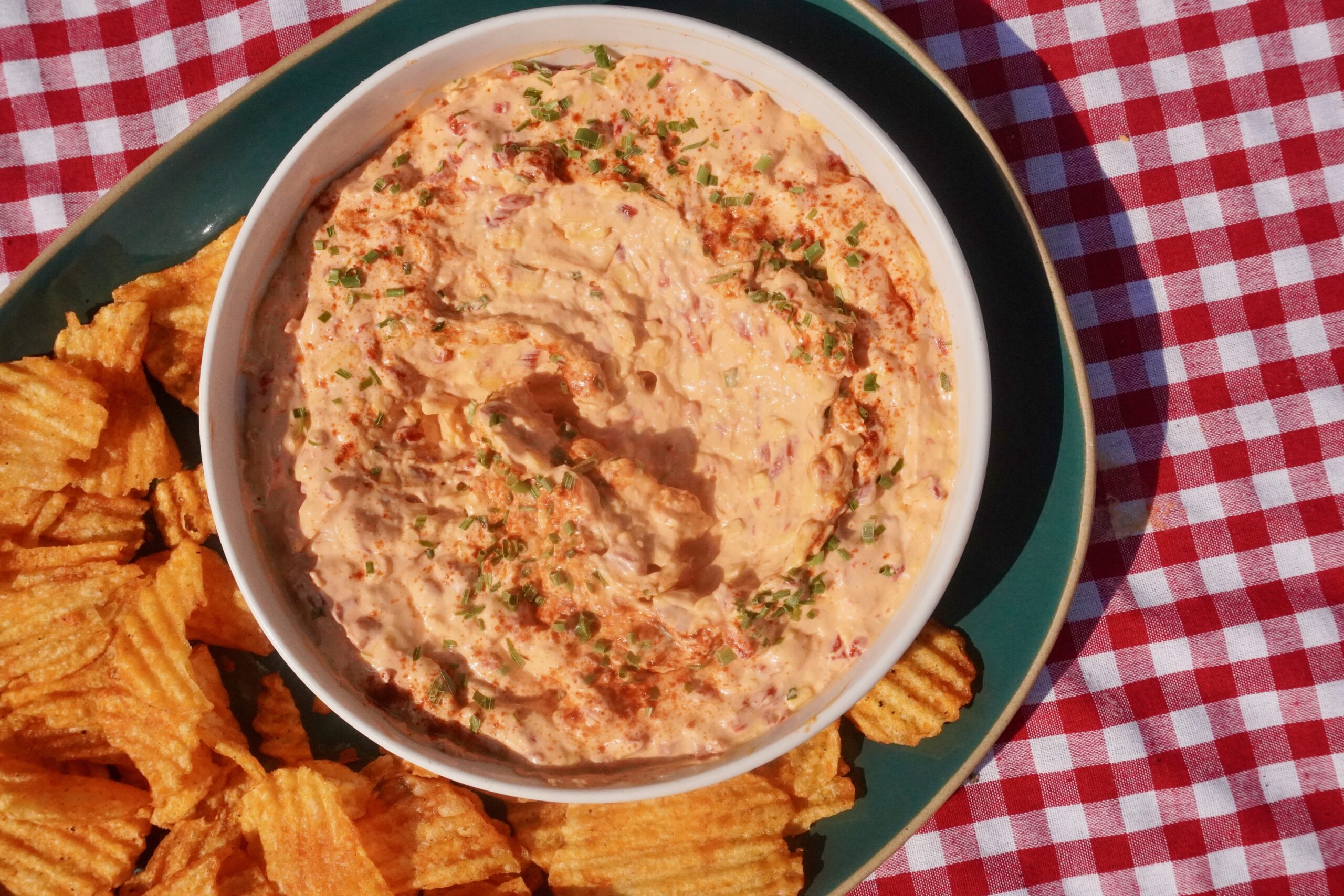 lose-up of creamy pimento cheese swirled in a white bowl and garnished with paprika and fresh chives