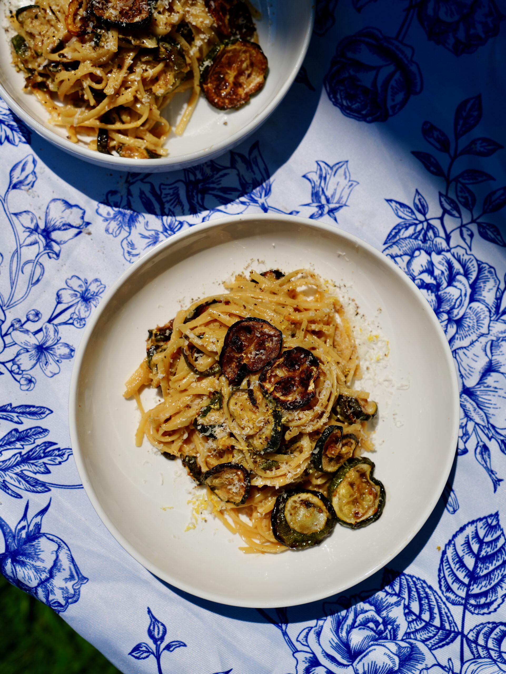 Overhead view of miso Alfredo linguine with roasted zucchini on a blue floral tablecloth