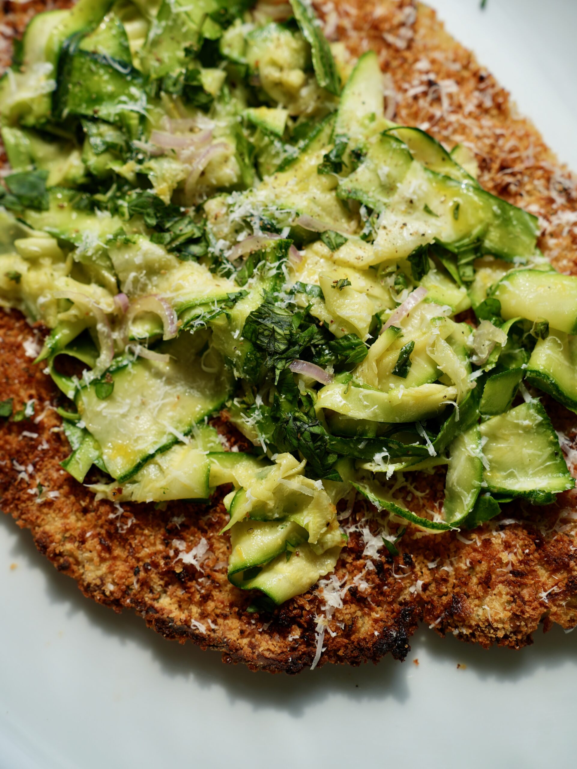Close-up of giant zucchini Parmesan chicken cutlet topped with shaved zucchini salad