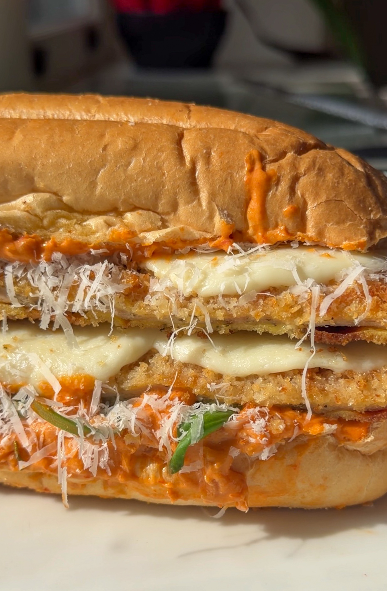 Close-up of spicy vodka chicken cutlet sandwich with melted mozzarella, crispy chicken cutlet strips, Parmesan, basil, and vodka sauce