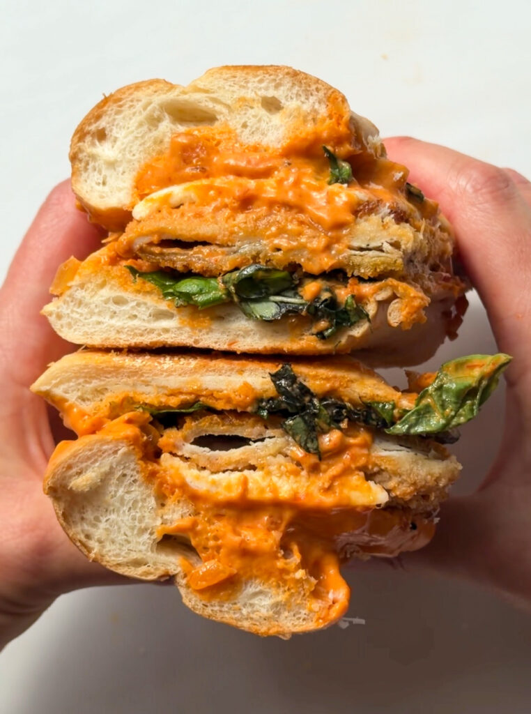 Spicy vodka chicken cutlet sandwich cut in half with melted mozzarella, basil, Parmesan, and vodka sauce on a hoagie roll