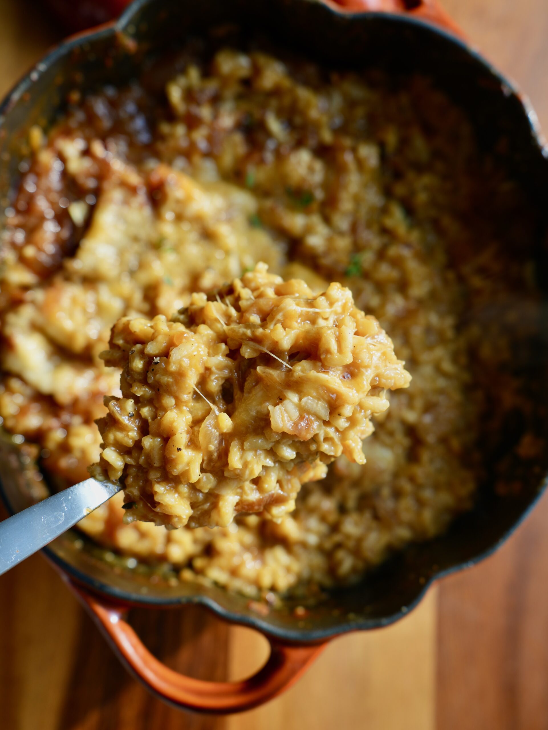 Spoonful of creamy French onion pumpkin risotto with caramelized onions and melted cheese lifted above the pot.