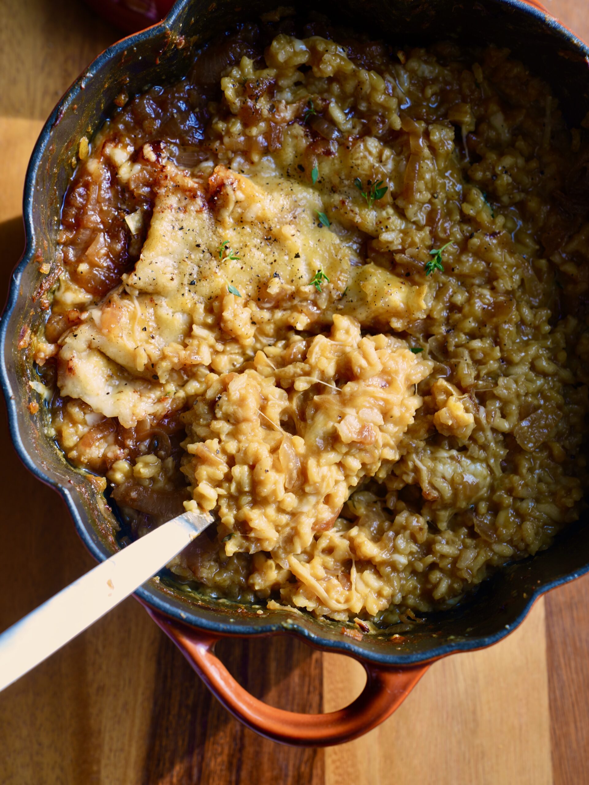 French onion pumpkin risotto with broiled cheese, caramelized onions and thyme in an orange pumpkin cocotte.