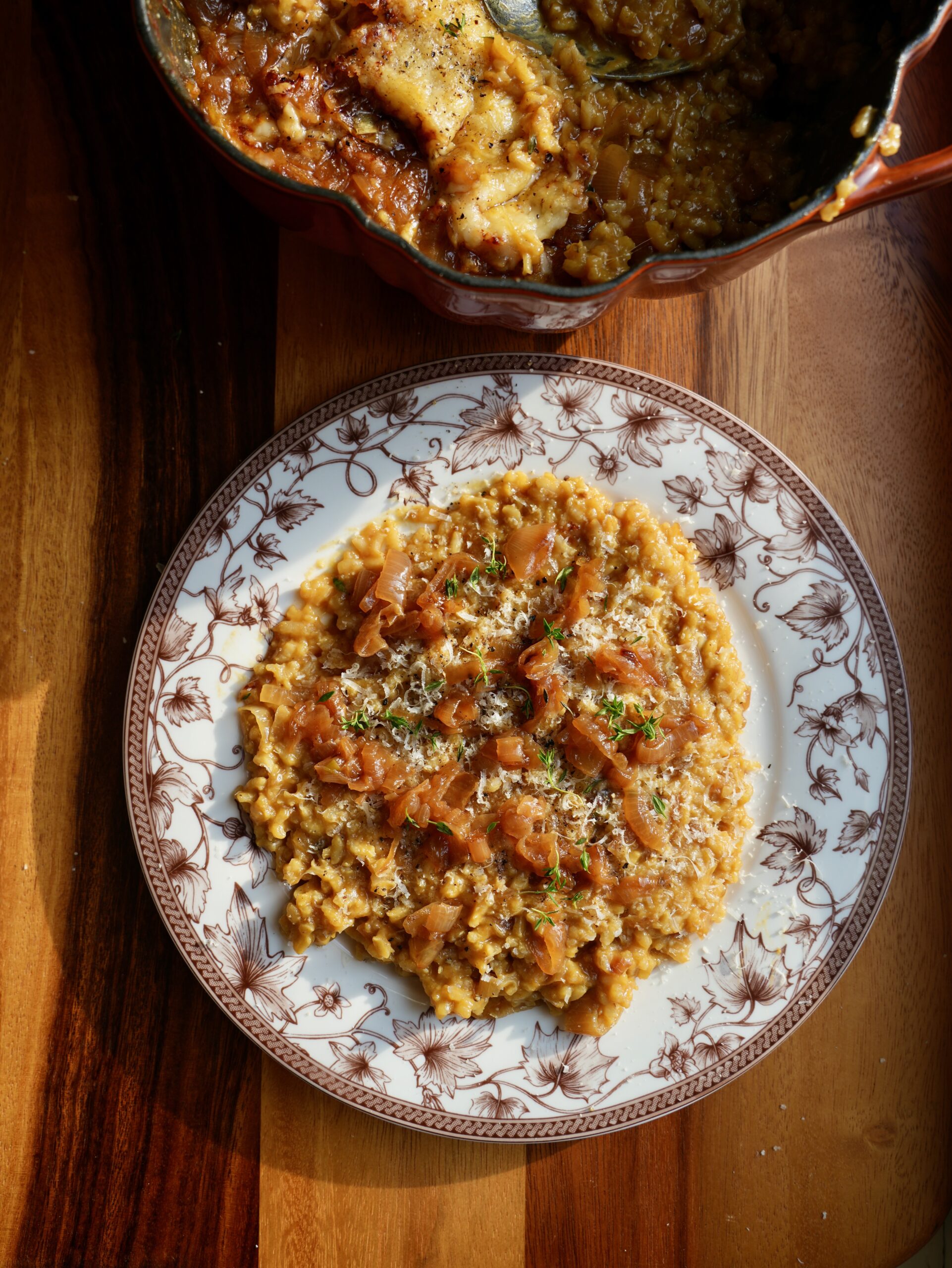 Plate of French onion pumpkin risotto topped with caramelized onions, grated cheese and thyme beside the serving cocotte.