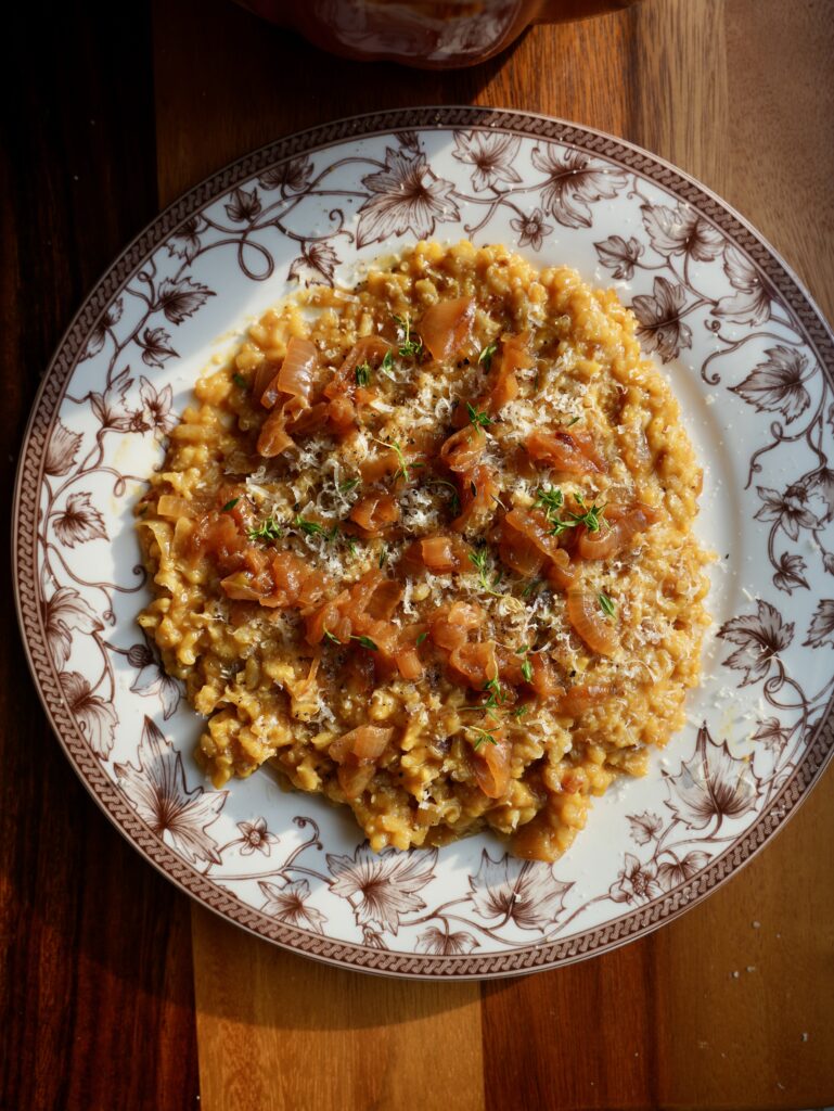French onion pumpkin risotto topped with caramelized onions, grated cheese and fresh thyme on a floral plate.