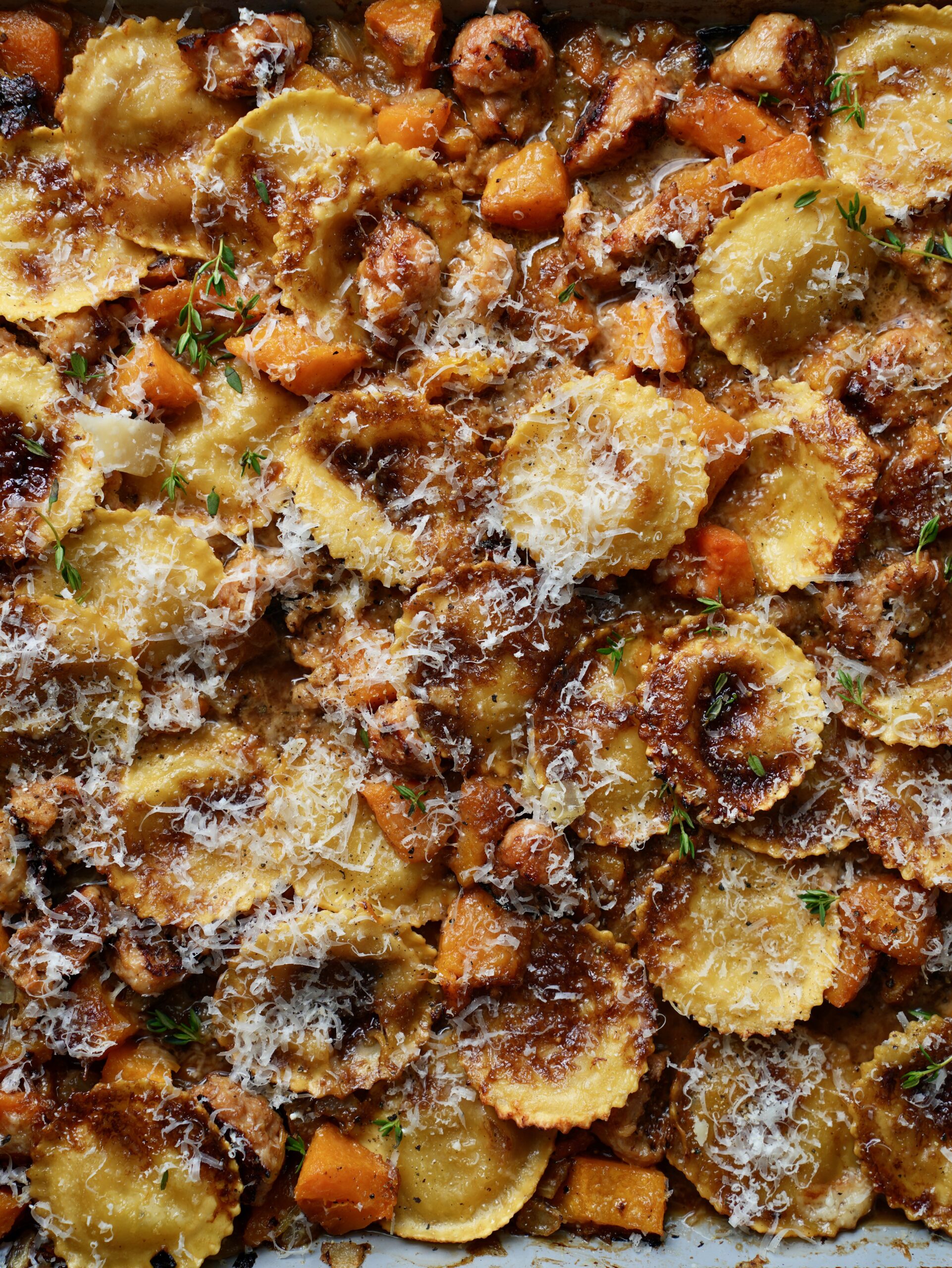 Overhead close-up of sheet pan ravioli, sausage and butternut squash with crisp browned edges, Parmesan and thyme.