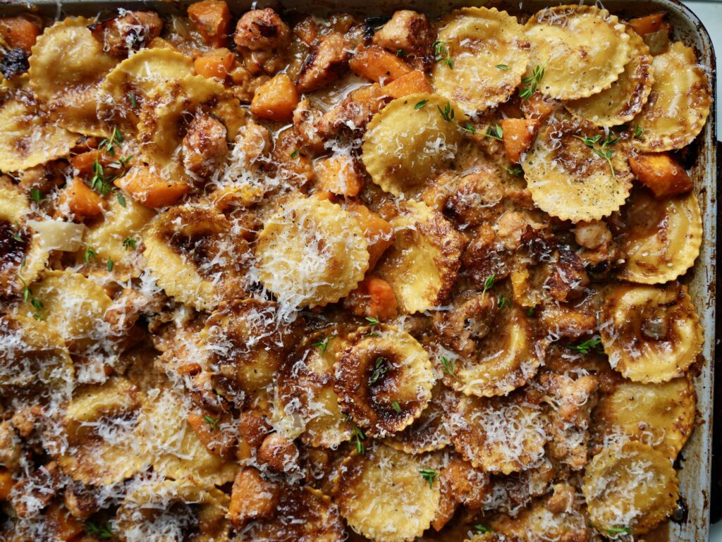Sheet pan filled with ravioli, caramelized butternut squash and browned sausage in sauce with Parmesan and thyme.